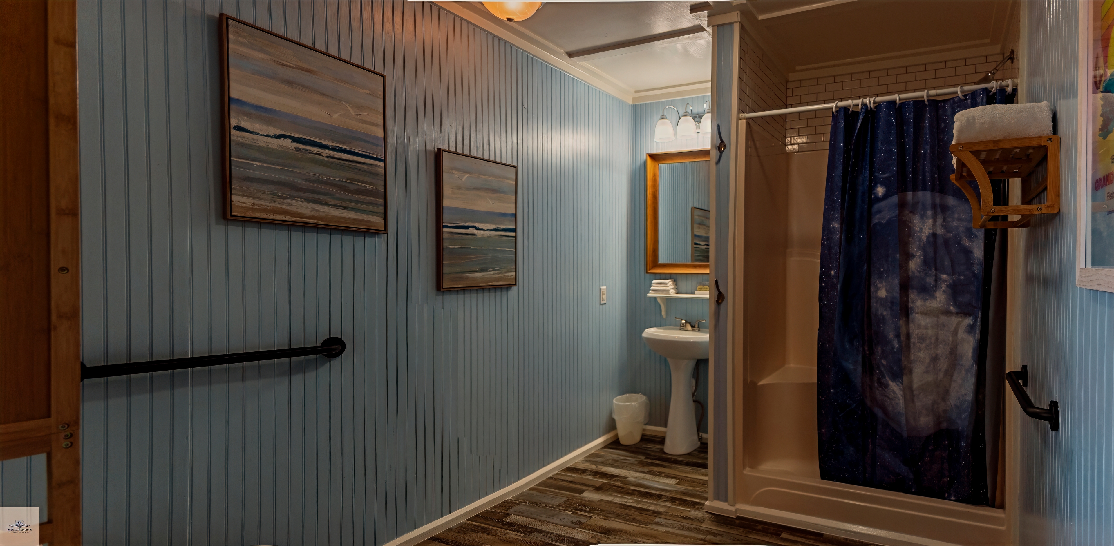 An accessible bathroom with light blue beadboard walls, a pedestal sink, and a white shower stall with a dark blue curtain.