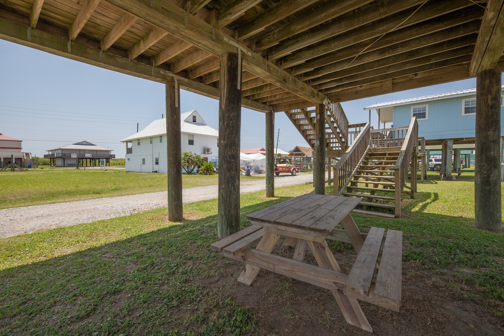 Shaded wooden picnic table under a raised coastal stilt house.