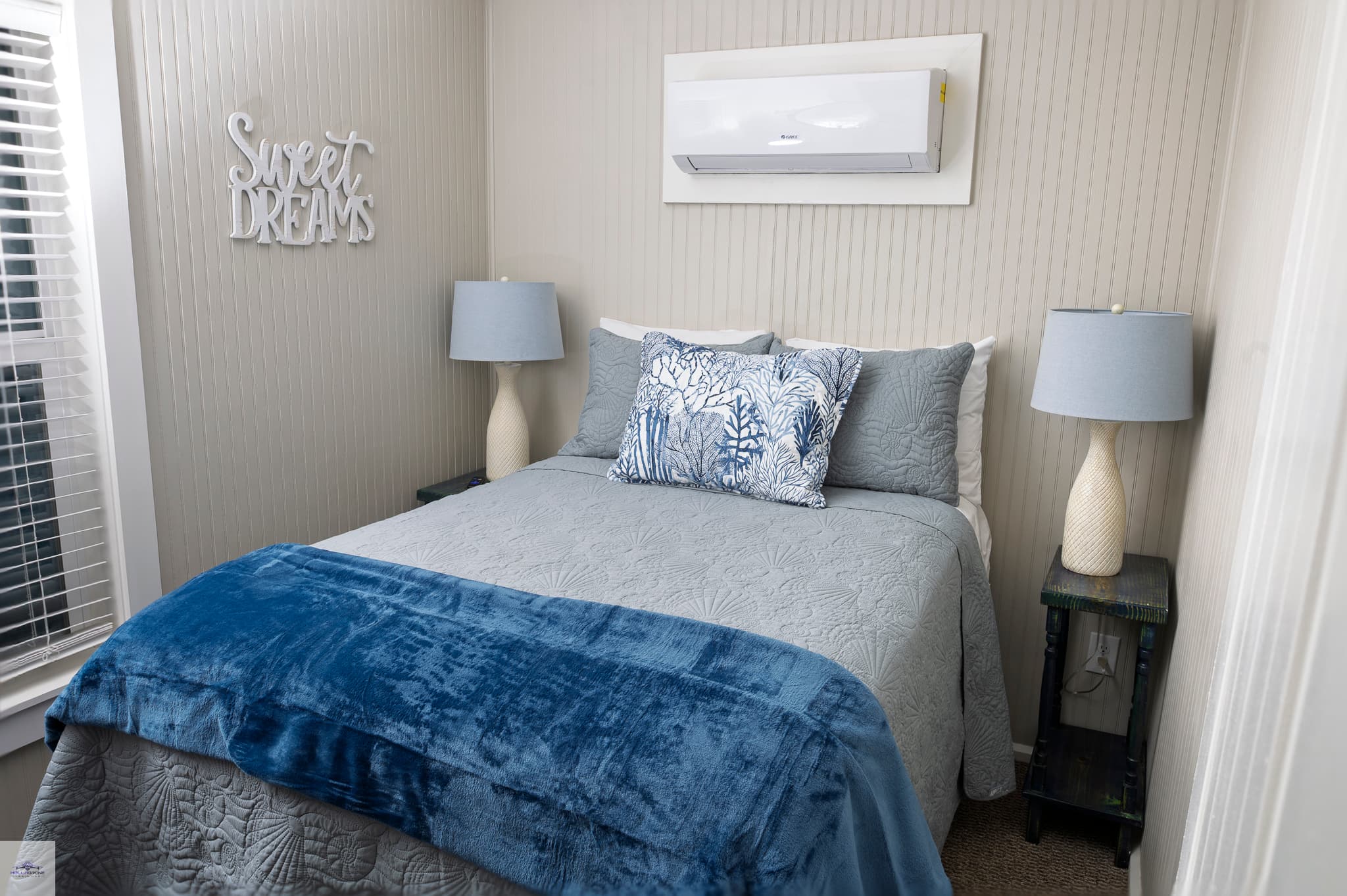 bedroom featuring a bed with grey and blue bedspread, and 2 lamps on either side