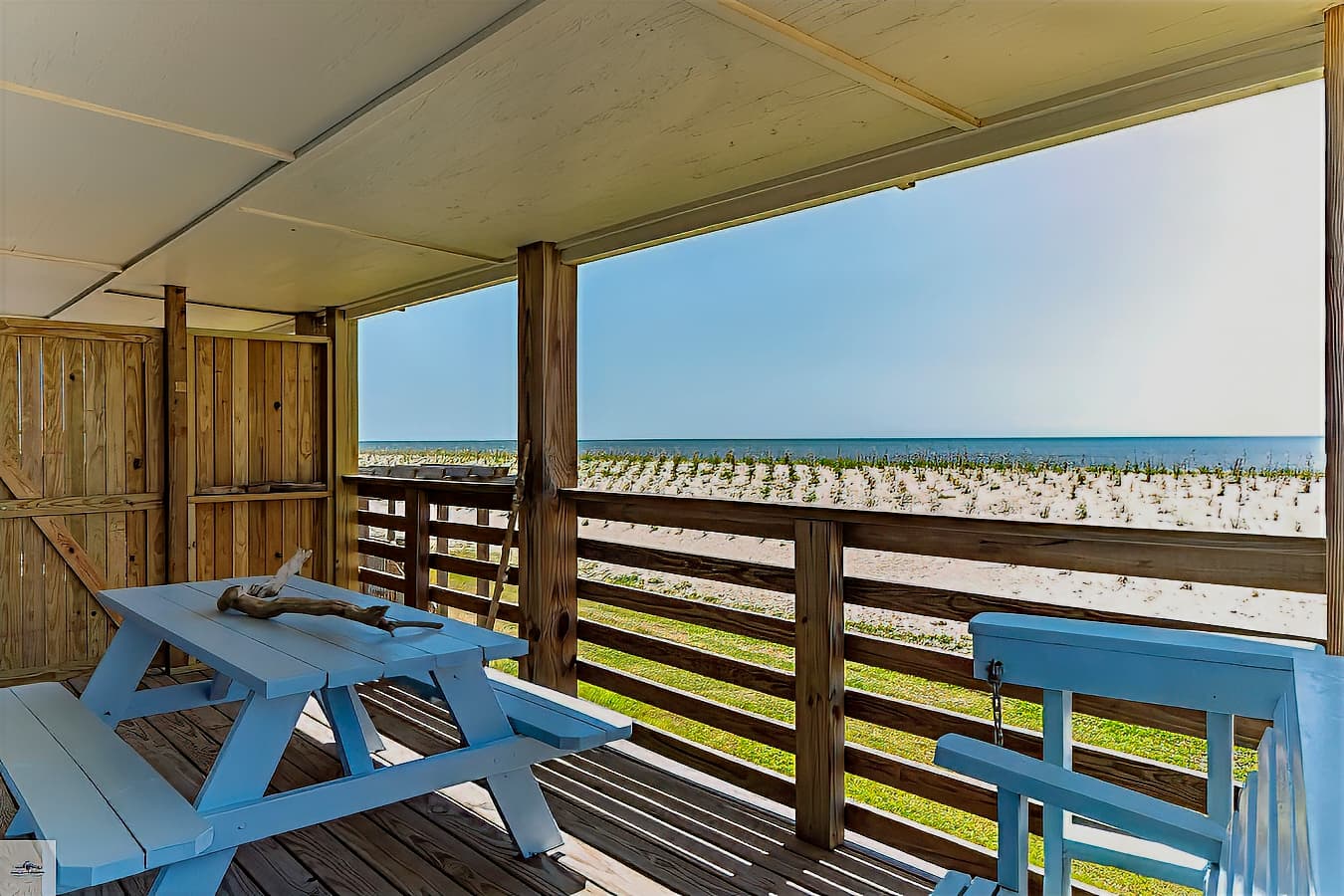 A covered porch with a light blue picnic table and a stunning, unobstructed view of the gulf and the sandy beach beyond the railing.