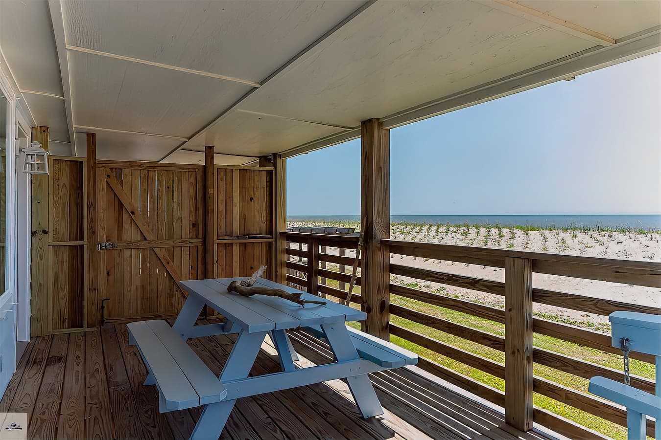 A covered porch with a light blue picnic table and a stunning, unobstructed view of the gulf and the sandy beach beyond the railing.