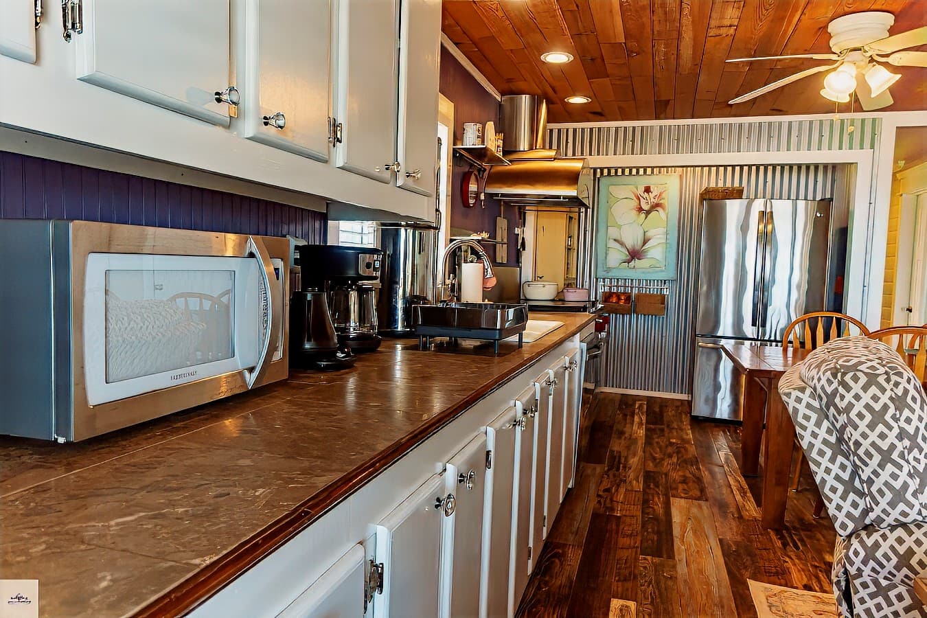 A close-up of a kitchen counter with white cabinets, a microwave, and a coffee maker. A stainless steel fridge is visible in the background.