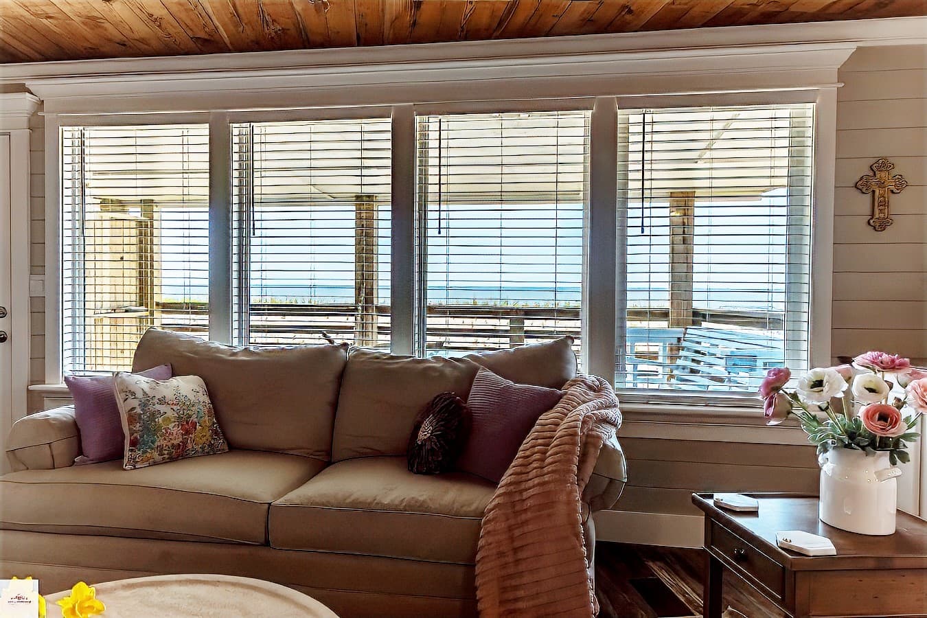 A beige sofa with pink and purple pillows is positioned in front of a bank of three windows, offering a bright view of the gulf beyond.