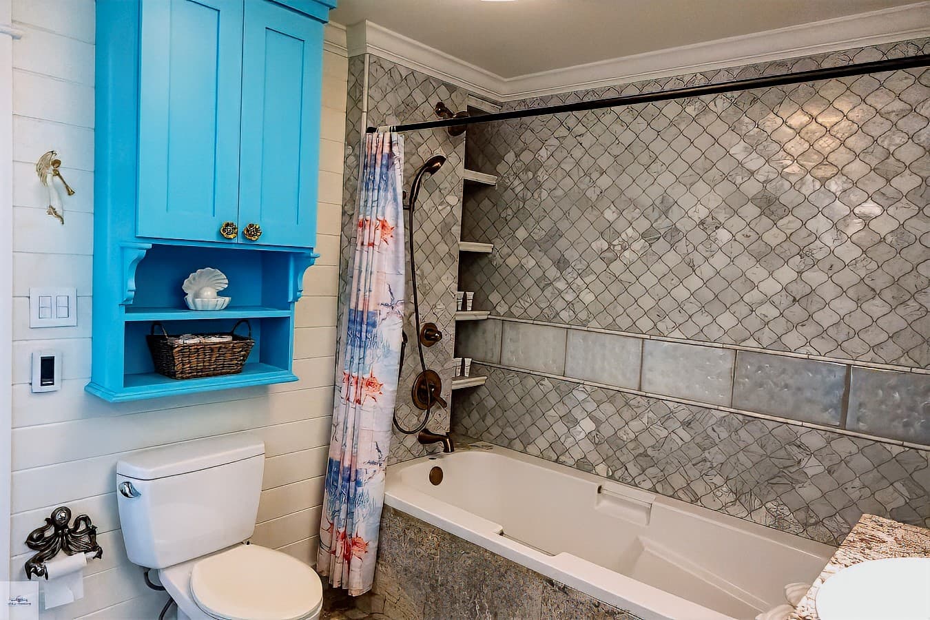 A colorful bathroom with a turquoise cabinet above the toilet, a tub/shower with mosaic tile surround, and built-in vertical shelving.