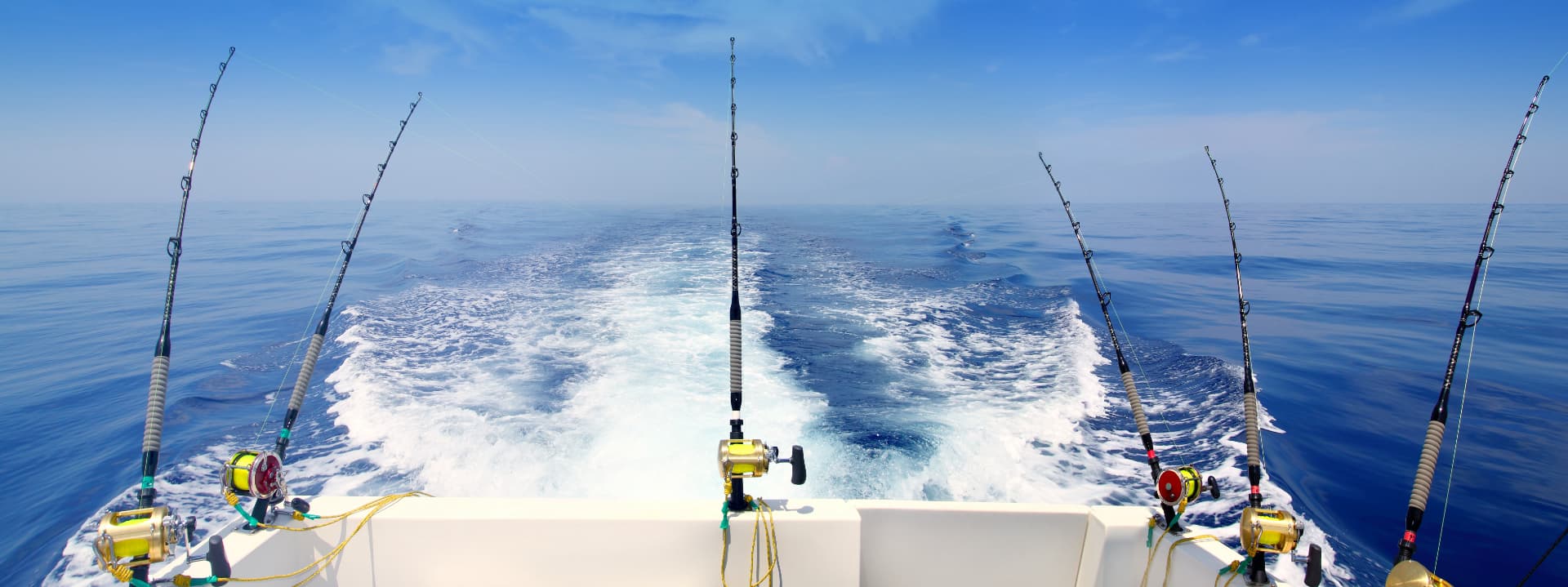 Fishing rods positioned on a boat, trailing a wake on a calm ocean.