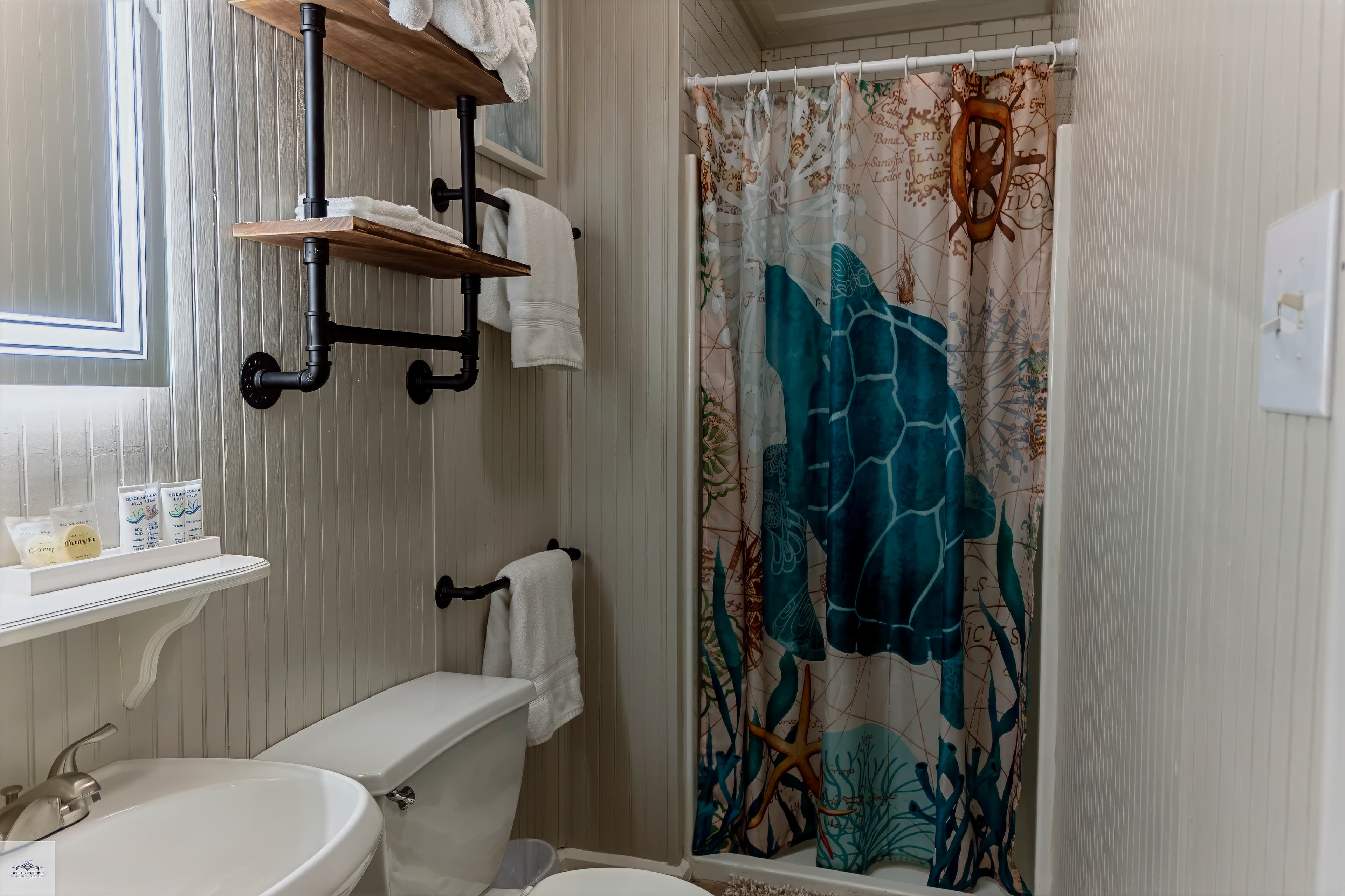 A stylish bathroom featuring a turtle-themed shower curtain, wooden shelves, and neatly arranged towels.