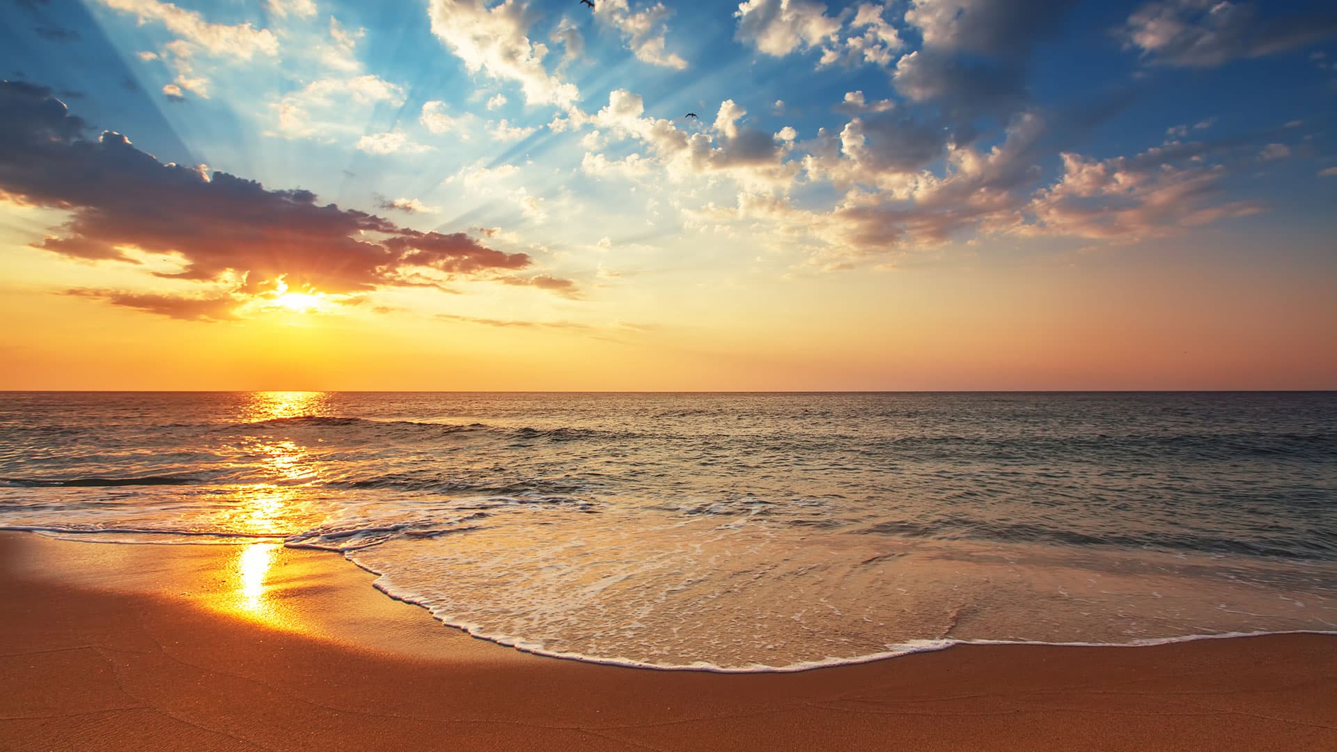 Sunset over a tranquil beach with gentle waves.