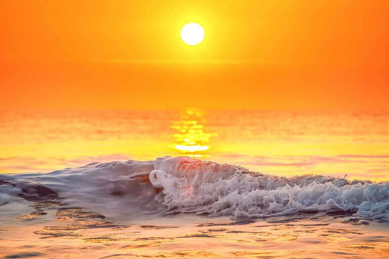 A vibrant sunset over a calm ocean wave.