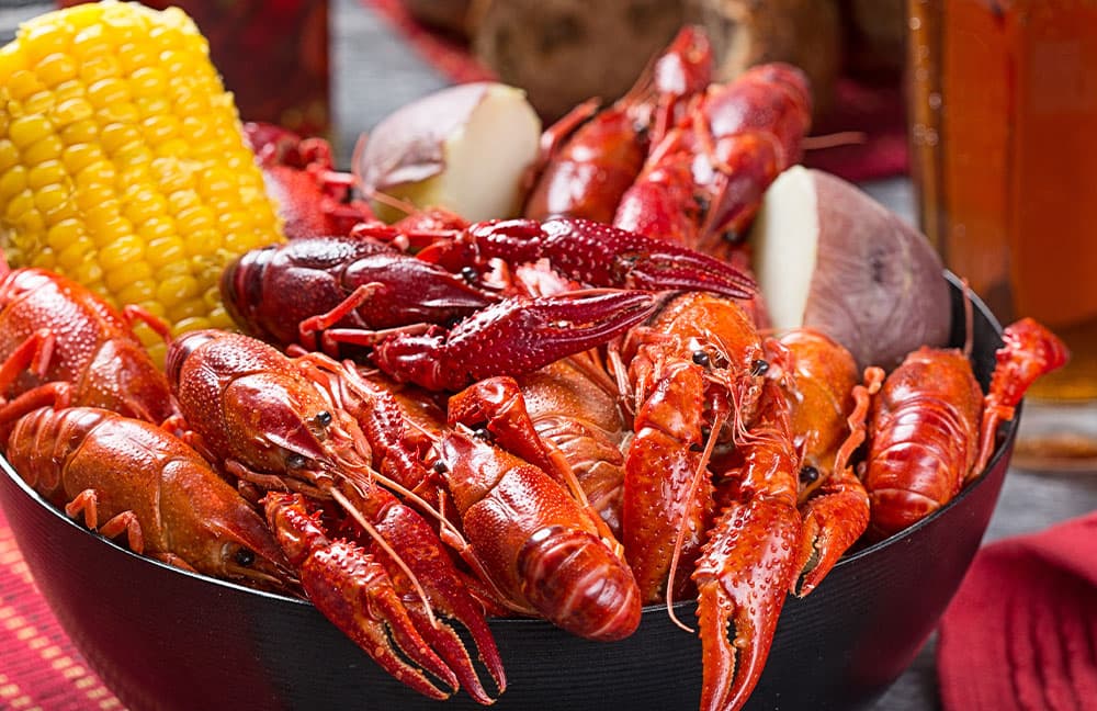 A black bowl filled with various cooked crawfish, yellow corn, and pieces of potato.