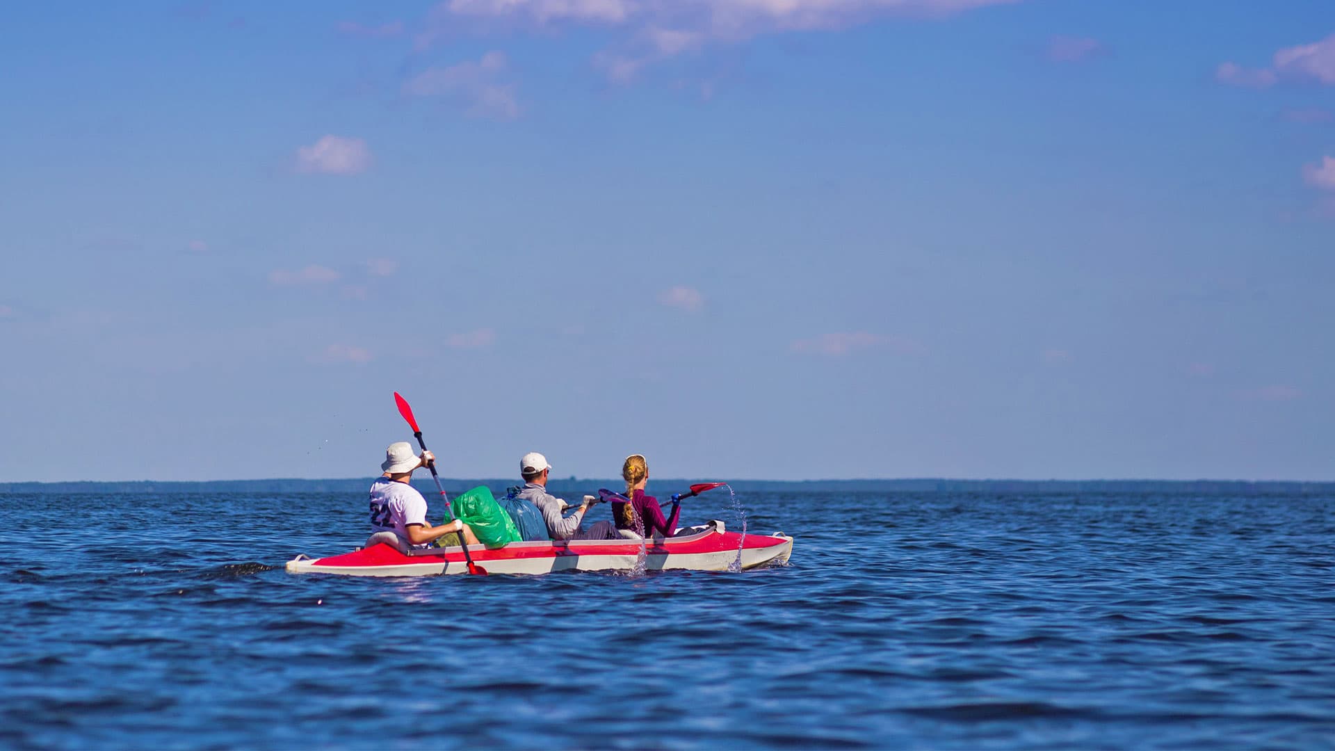 Three people in a kayak on a calm body of water under a blue sky.