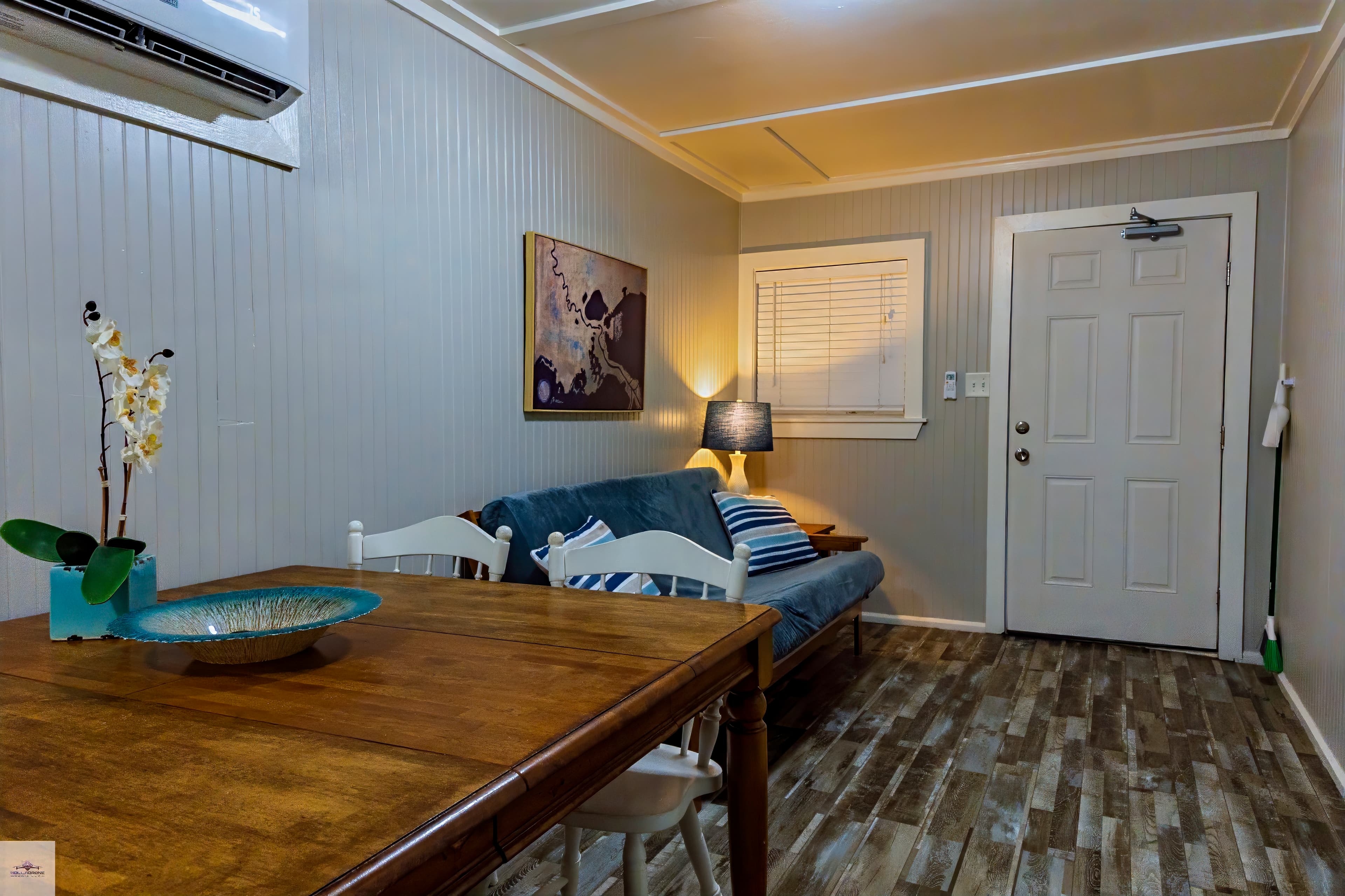 The living area of a 2-bedroom suite features a wooden dining table, a blue futon with a lamp, and light gray walls.