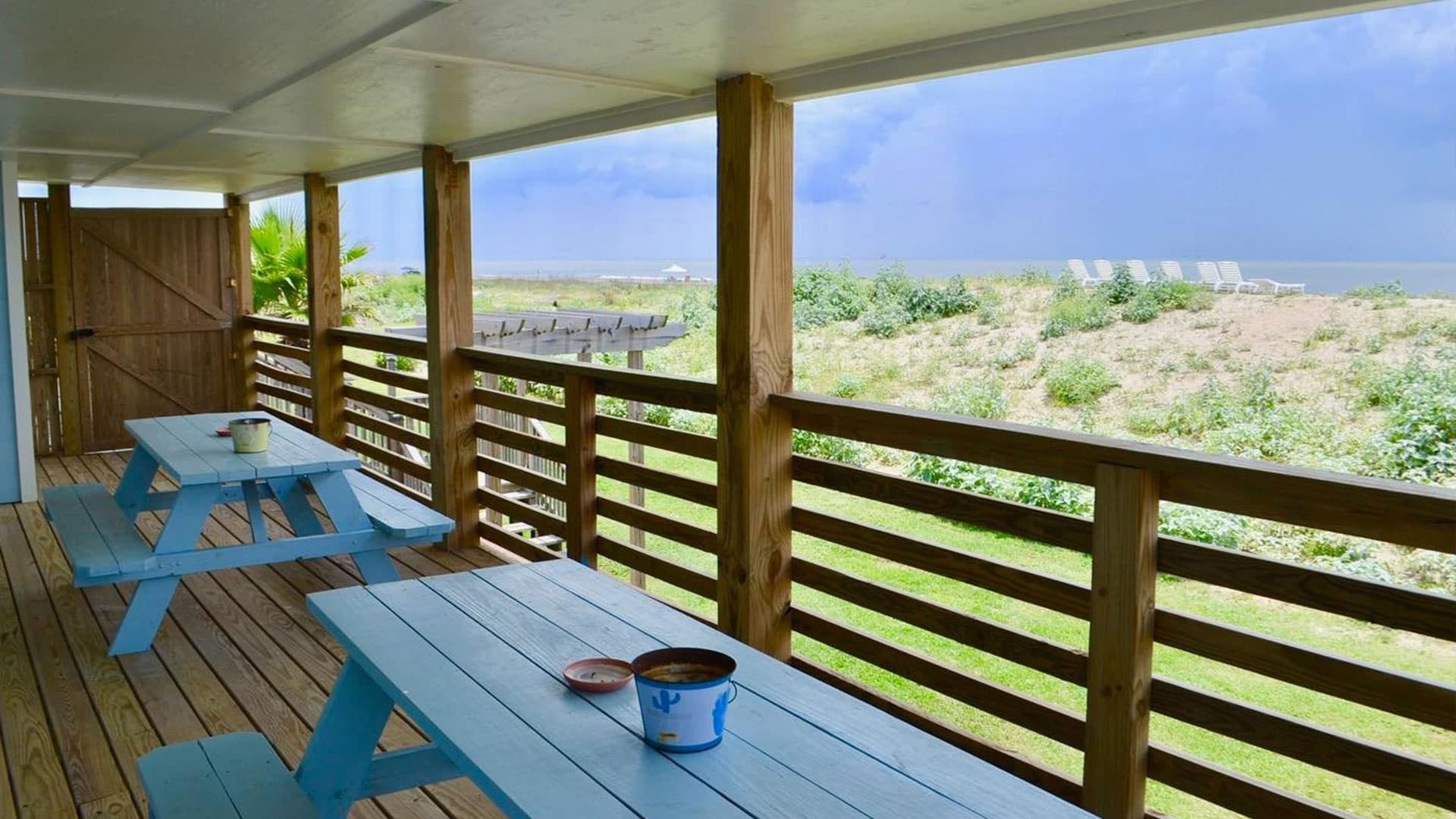Covered porch with blue picnic tables overlooking a grassy area and distant ocean.
