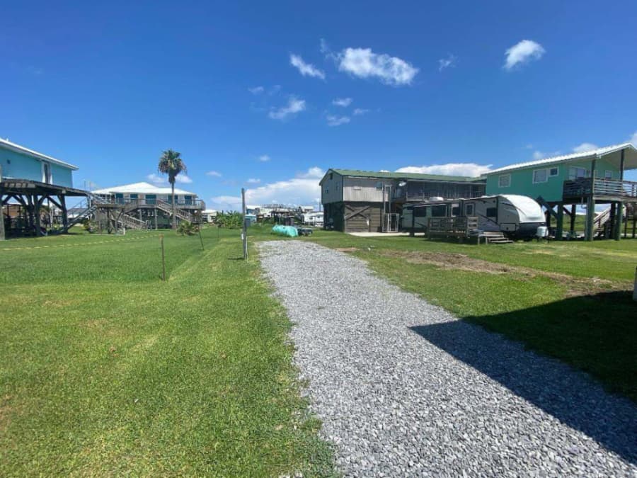A gravel pathway leads through a grassy area bordered by elevated homes under a clear blue sky.