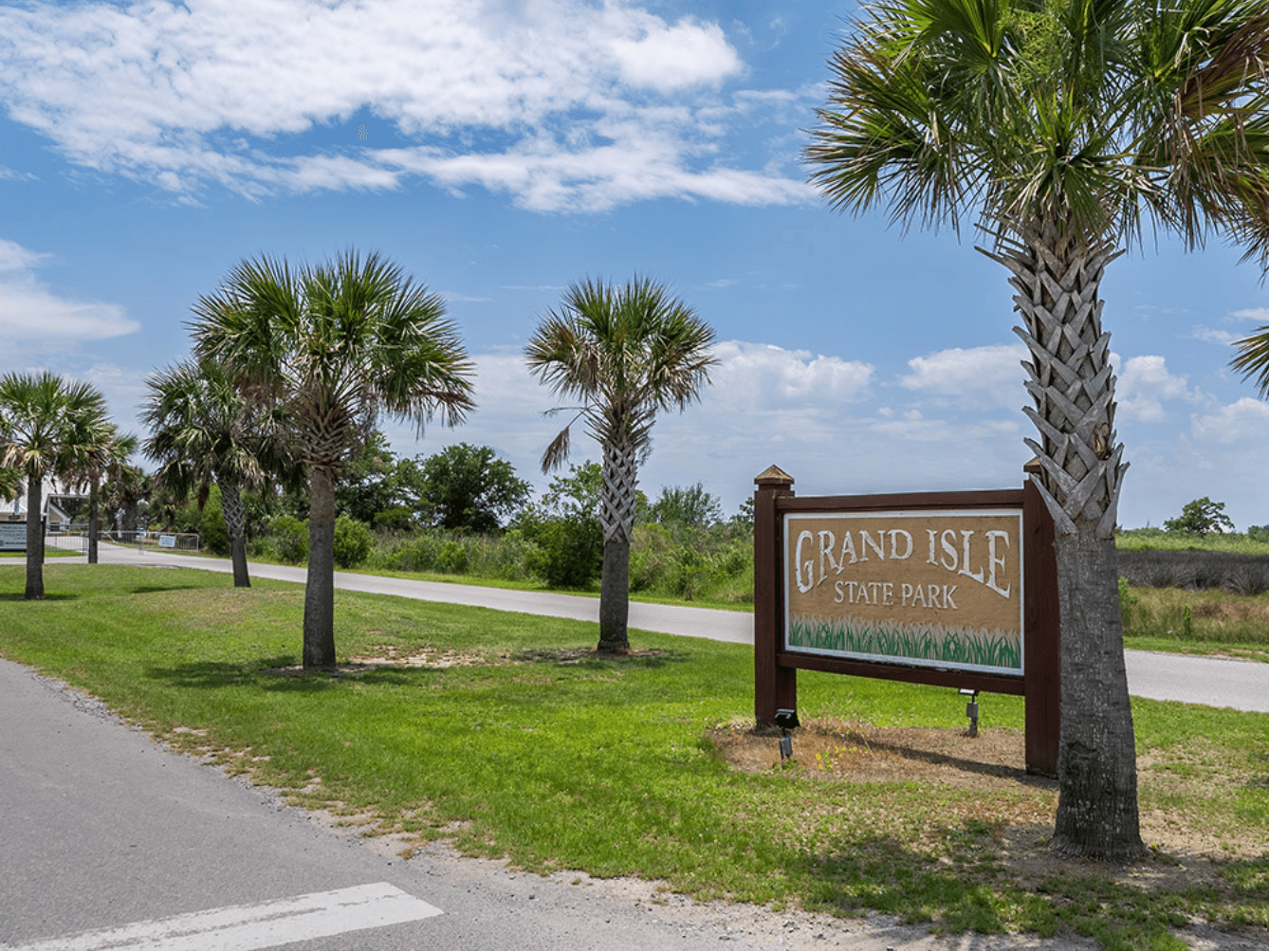 Grand Isle State Park entrance sign lined with palm trees under a blue sky