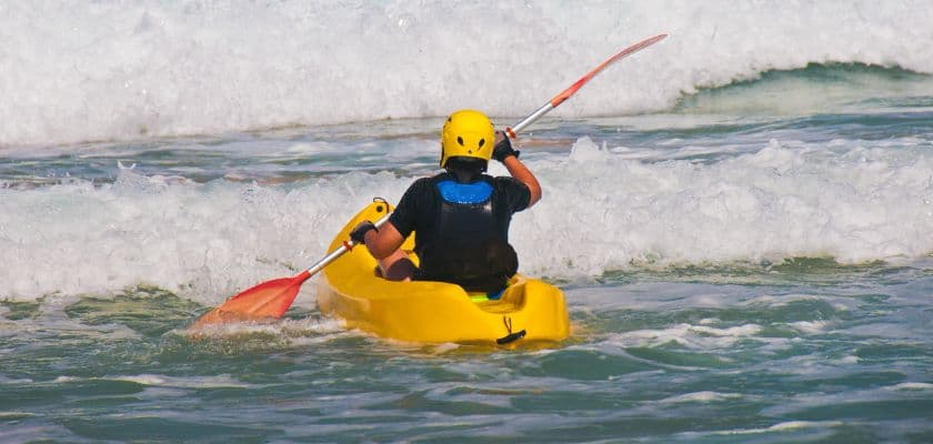 man kayaking in the surf with small waves rolling in